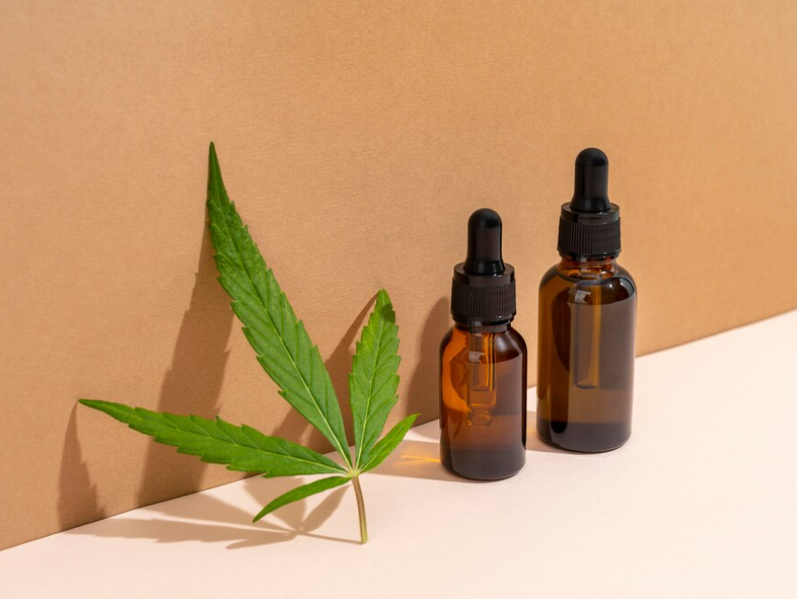 A cannabis leaf and two CBD oil dropper bottles against a beige background with shadows.