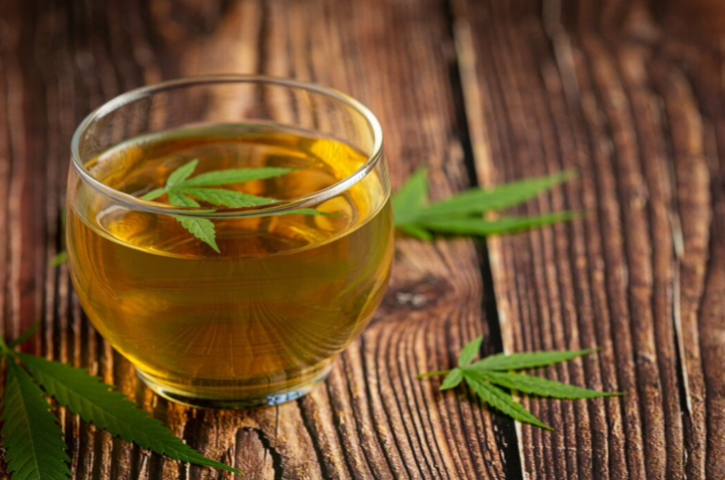 Glass of hemp tea with hemp leaves on wooden table