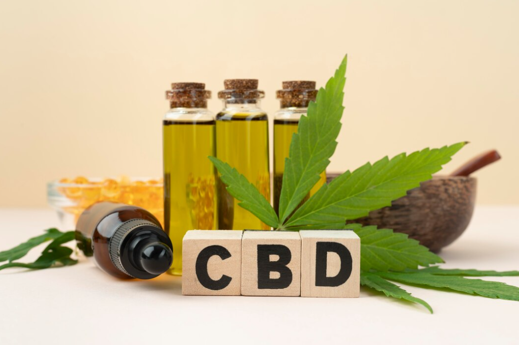 Bottles of CBD oil, fresh cannabis leaves, and wooden blocks spelling "CBD" arranged on a beige background.