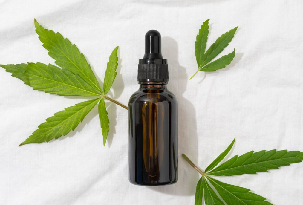 dark CBD oil dropper bottle flanked by fresh cannabis leaves on a white, linen-textured surface.