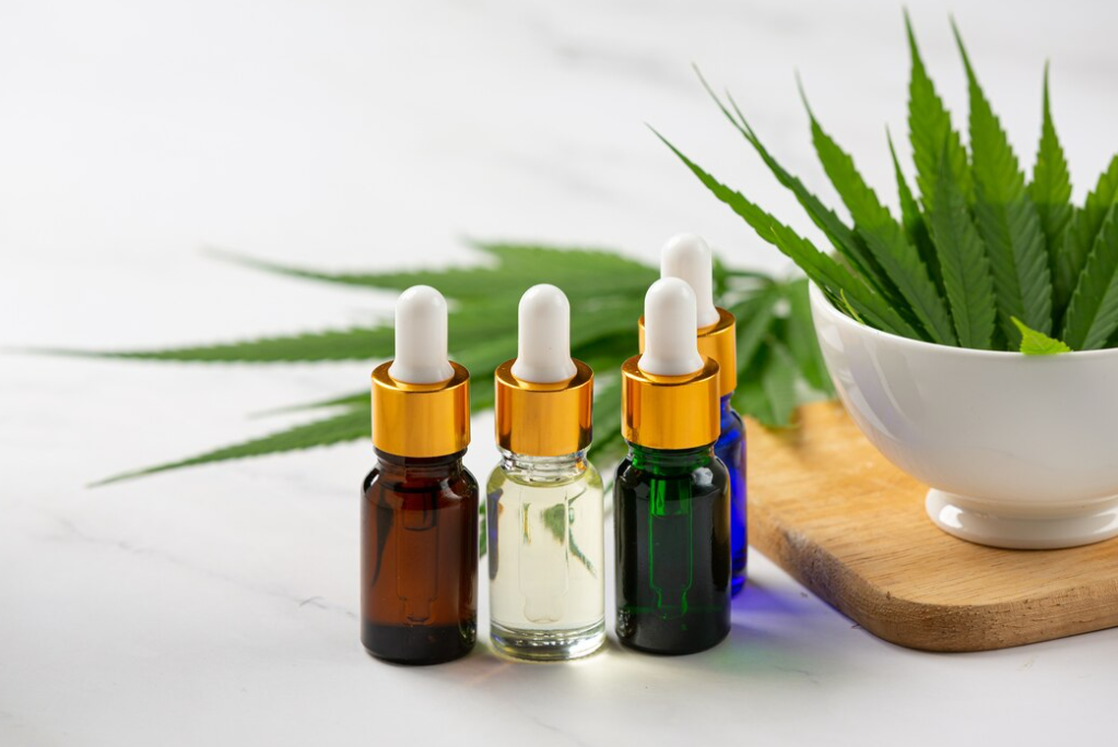 Three dropper bottles of CBD oil with cannabis leaves on a white marble surface.